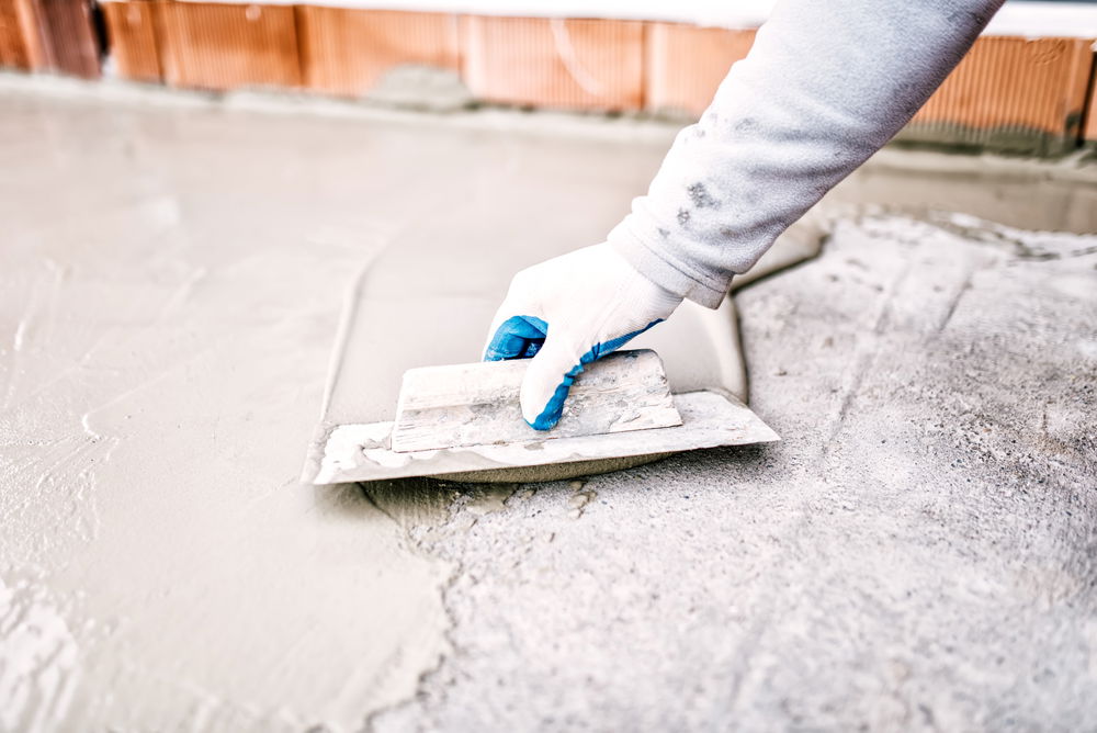 A constractor uses a trowel to repair a concrete floor.