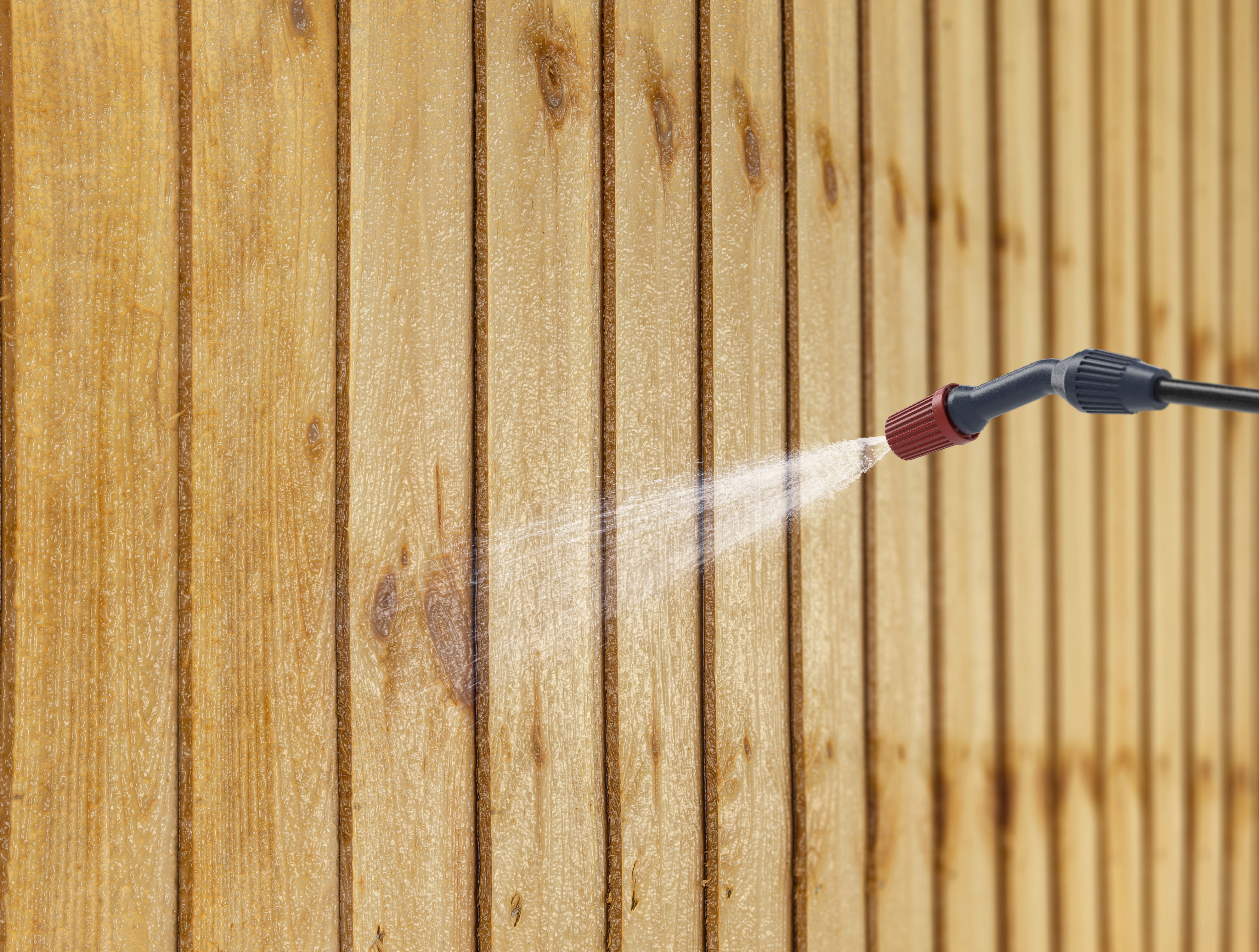 A gloved hand applies Roxil Wood Protection Cream on a wooden fence with a brush.