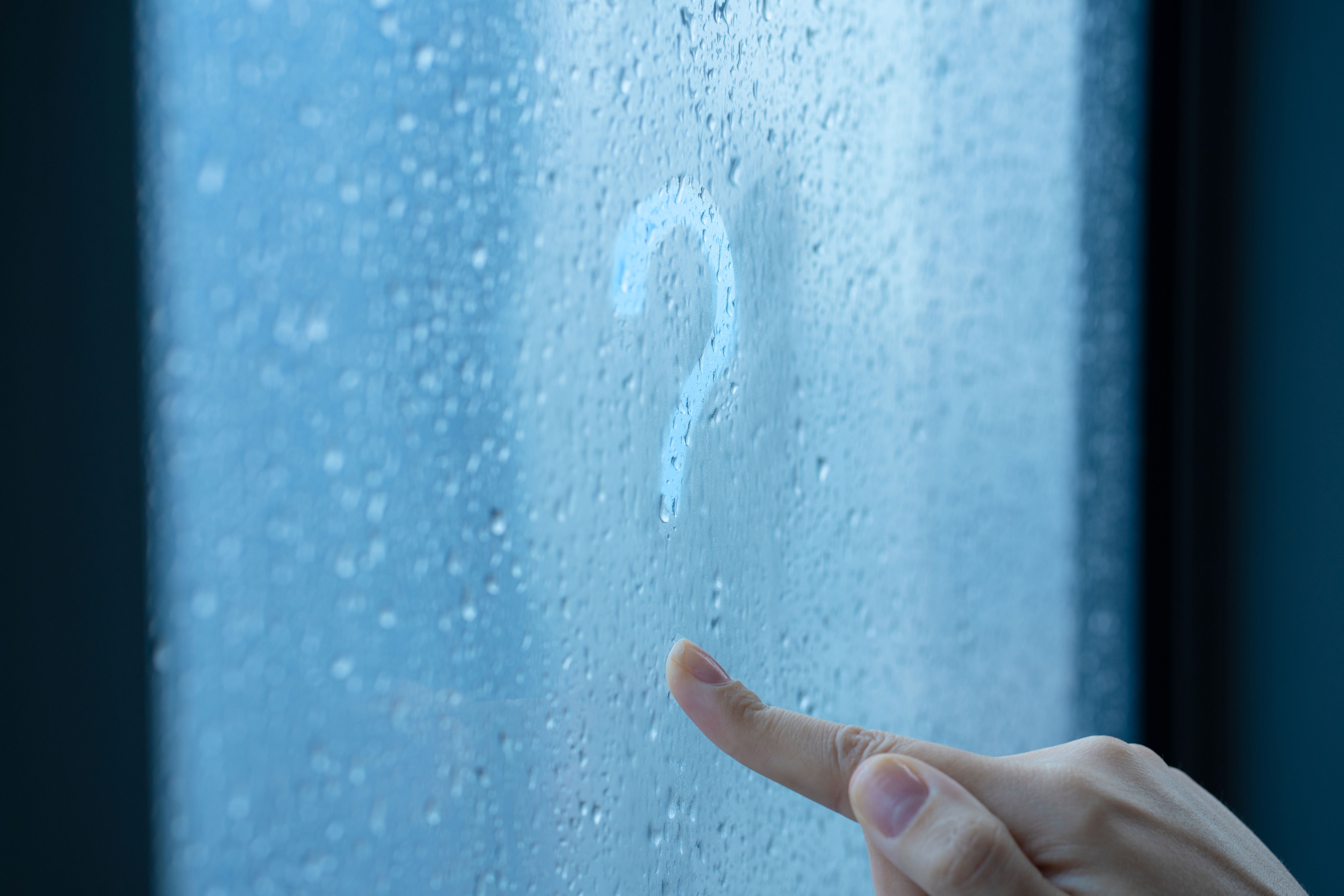 A finger draws a question mark in condensation on a window.