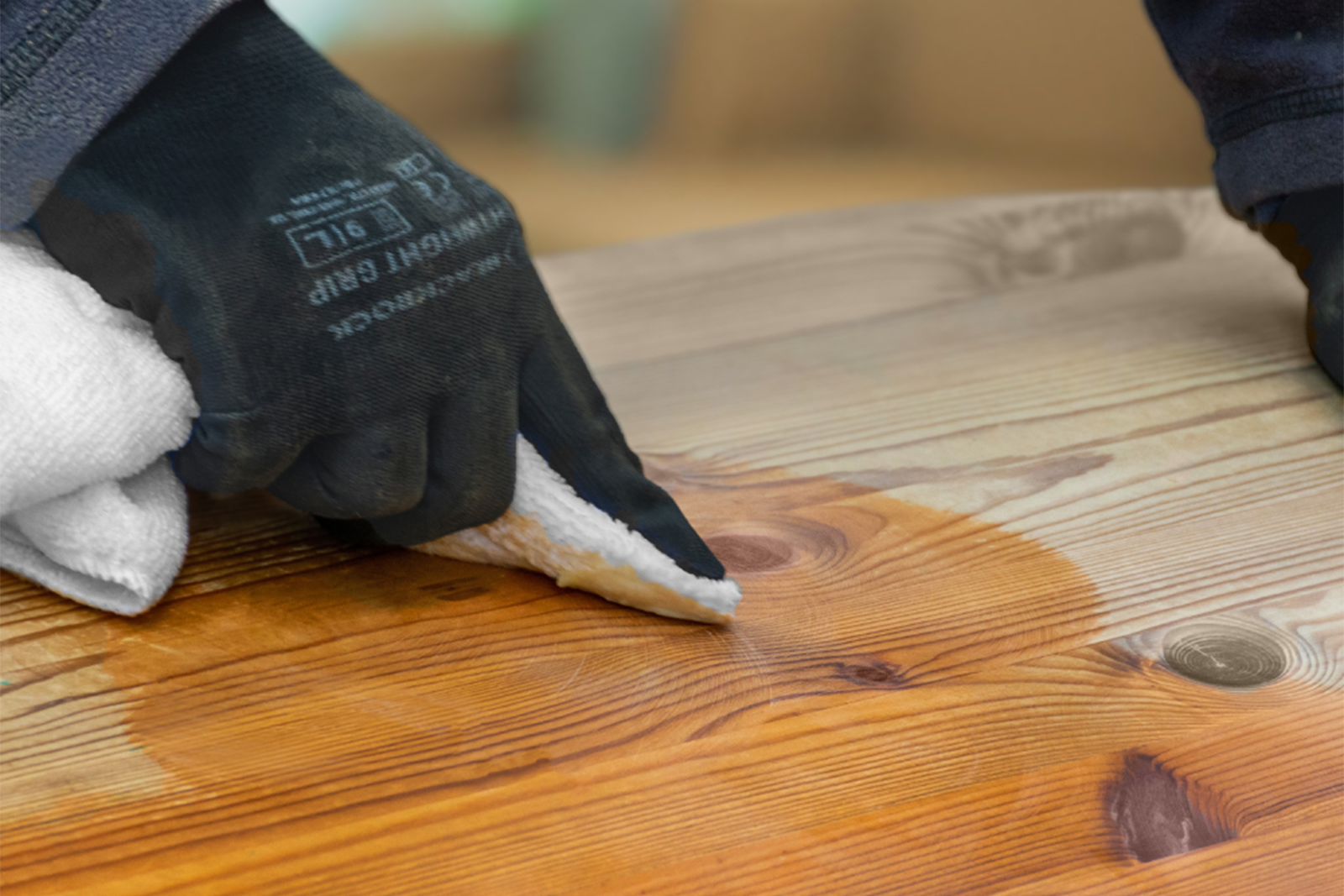 A hand applying a wax on a wooden table with a cloth.