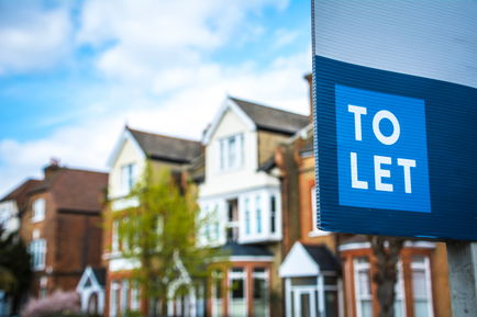 Foreground: A blue 'to let' sign. Background: A row of semi-detached UK townhouses.