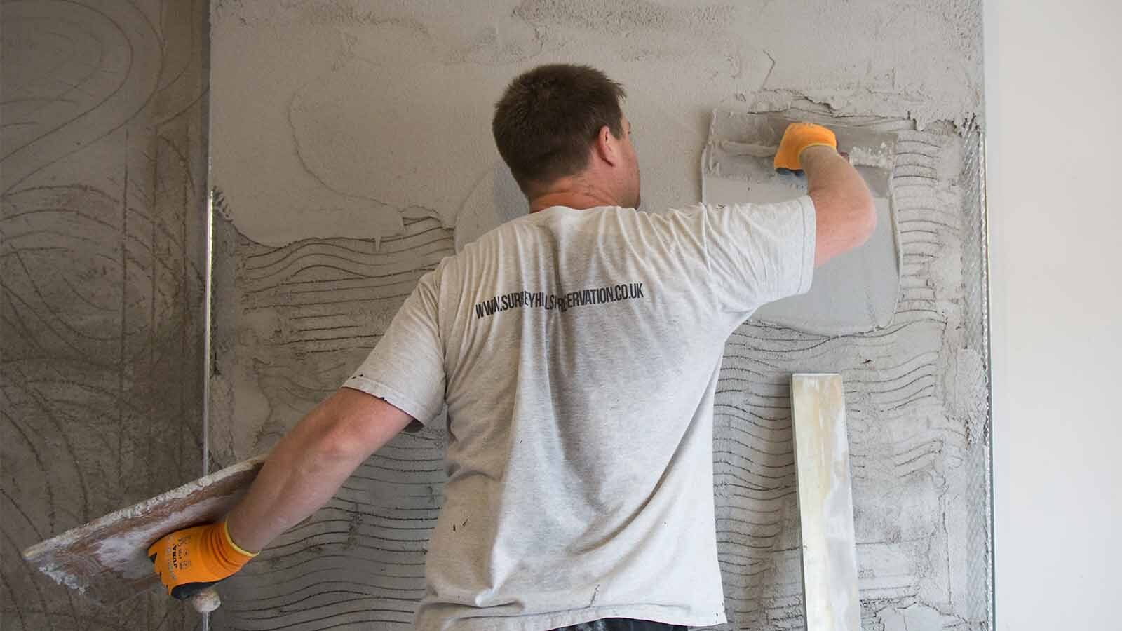 A plasterer applies damp-resistant plaster to a wall.