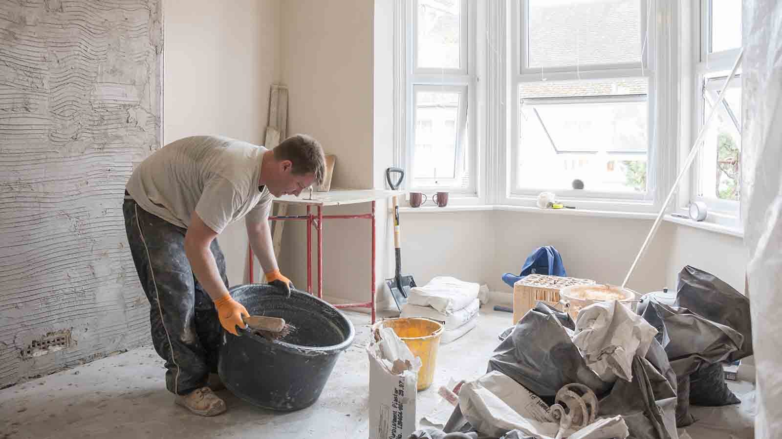 A contractor mixes damp-resistant plaster in a bucket.