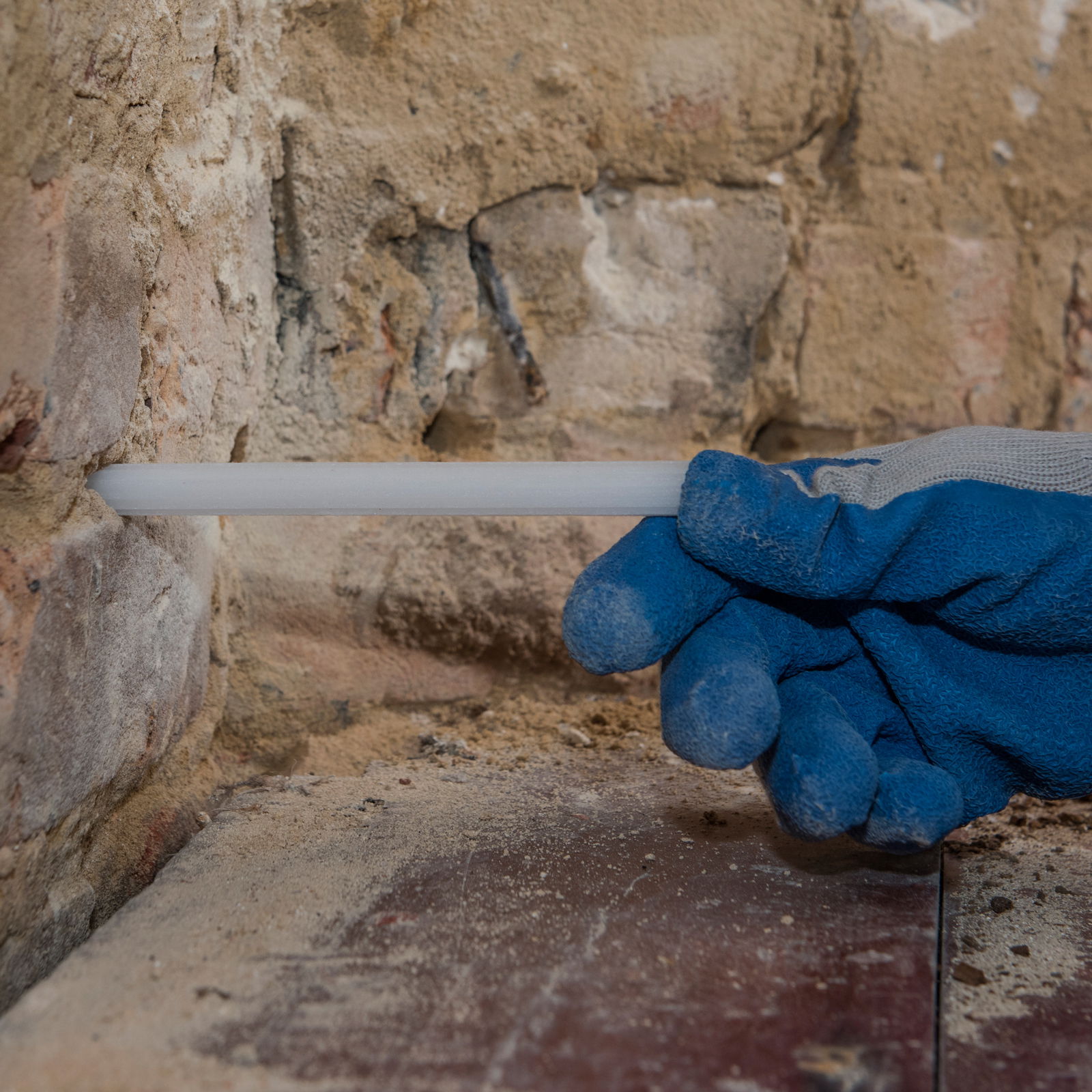 Someone wearing gloves and inserting rod in the wall.