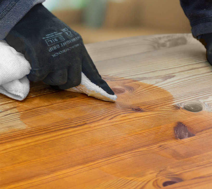 A person applying the Roxil Beeswax Wood Polish on a wooden table.